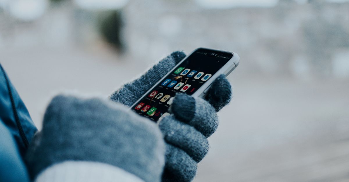 Close-up of hands using smartphone with gloves in winter, showing apps on screen.